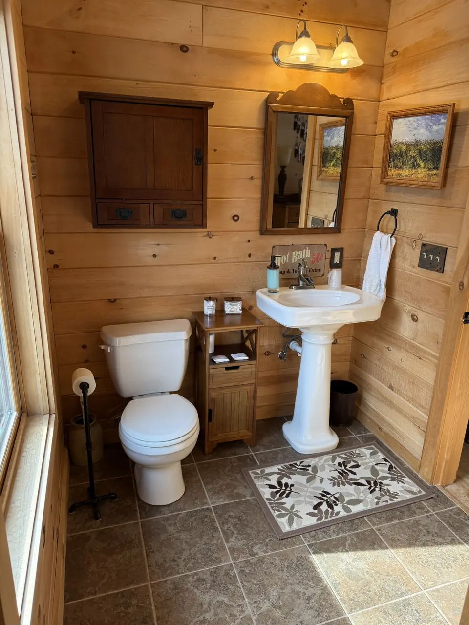 Guest bathroom with pedestal sink, framed mirror, and log walls