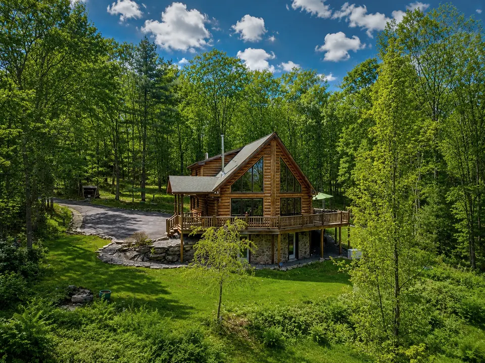 Drone view of the log cabin and driveway set among tall trees in Glen Spey, New York