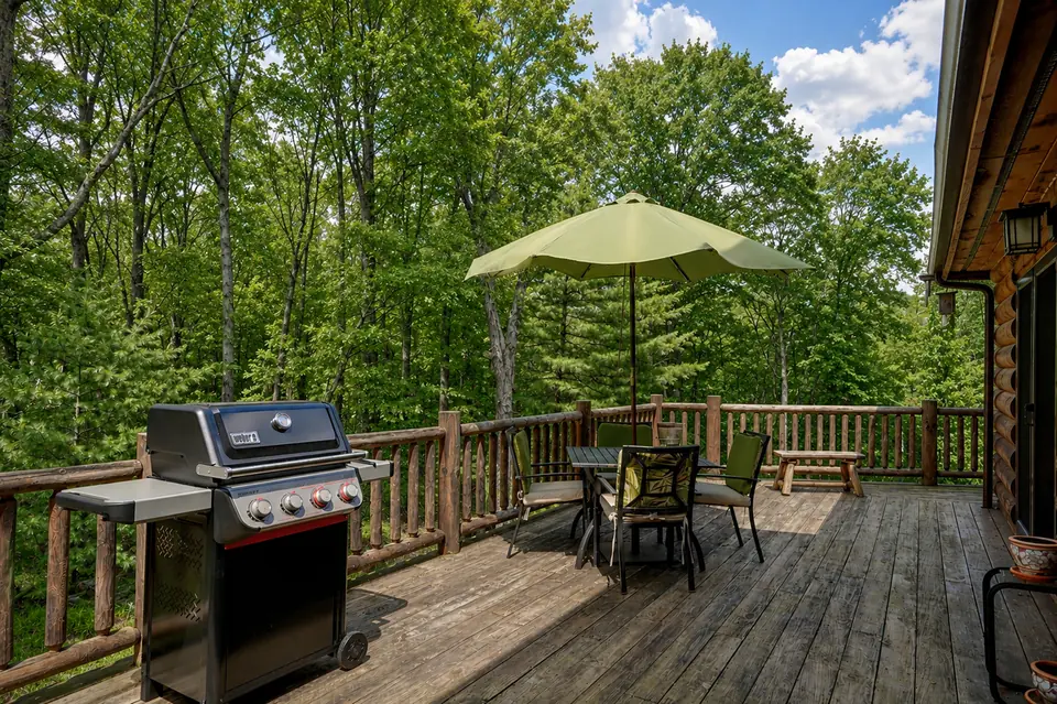 Deck with a gas grill, umbrella, and outdoor dining table overlooking the woods
