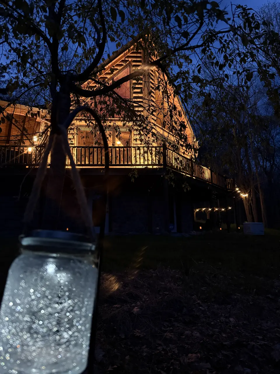Lantern jar glowing on the path at night with the cabin lit beyond