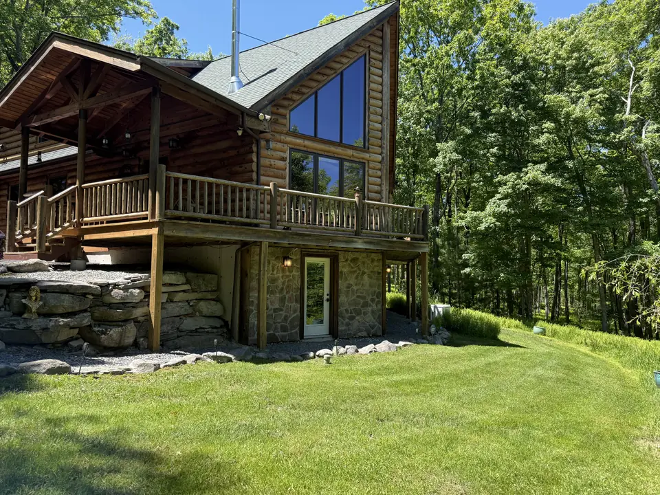 The log cabin deck above a wide sunny lawn with the woods beyond
